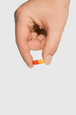 Red and yellow pill held in a hand
