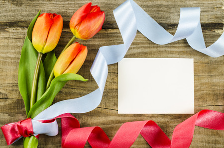 Empty postcard, colorful flowers and ribbon on wooden backgroundの写真素材