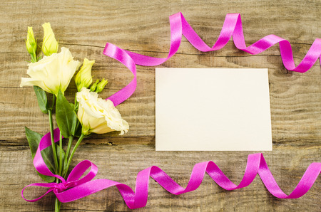 Empty postcard, colorful flowers and ribbon on wooden backgroundの写真素材