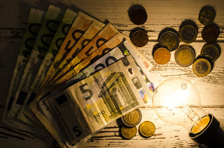 Glowing light bulb with money on wooden backgroundの写真素材