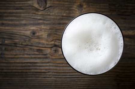 Glass of beer foam over wooden tableの写真素材