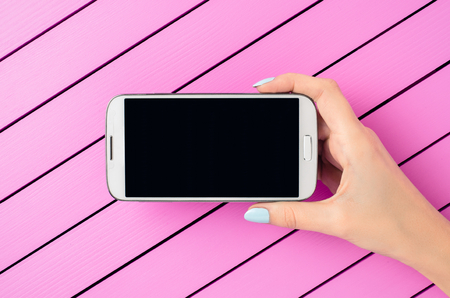 Female hand holding a white mobile phone over pink backgroundの写真素材