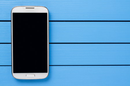White mobile phone with black screen on blue wooden backgroundの写真素材