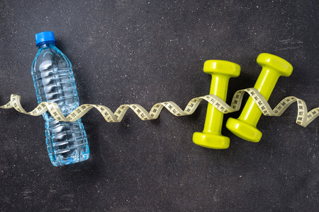 Fitness concept with dumbbells, water, tape measure and green apple on dark backgroundの写真素材