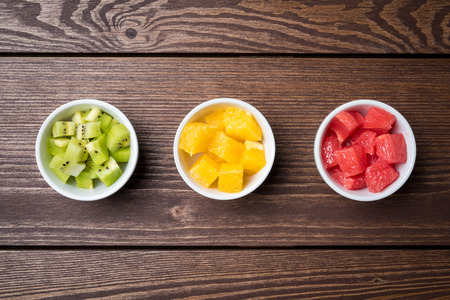 Cut fruits in white bowls on wooden tableの写真素材