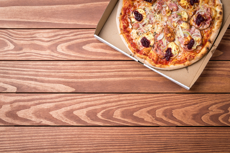 Pizza in a cardboard box on a wooden tableの写真素材