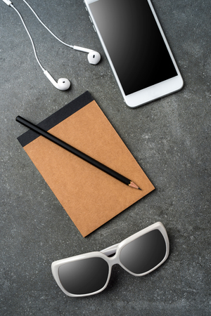 White smartphone, earphones, sunglasses and notebook on gray stone backgroundの写真素材