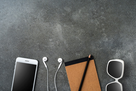White smartphone, earphones, sunglasses and notebook on gray stone background