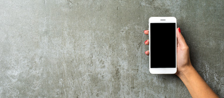 Female hand holding white mobile phoneの写真素材