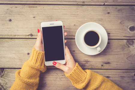 Woman using a white smartphone in a warm sweaterの写真素材