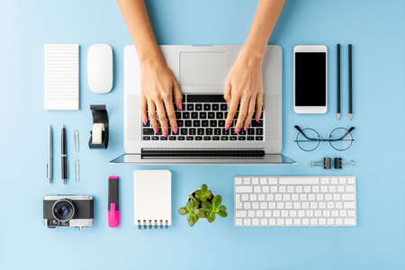 Woman's hands working on laptop on blue table with accessories. Modern workspace. Flat lay