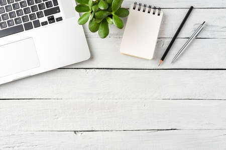 Laptop, notebook, pens and small succulent on white wooden desktop. Business background. Top view