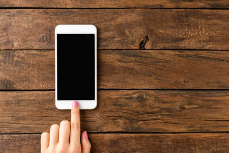 Woman's hand using smart phone with empty screen on rustic wooden background. Close up