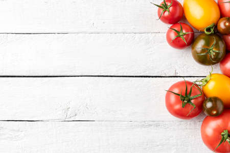 Overhead shot of different tomatoes on white wooden background with copyspace. Top viewの写真素材
