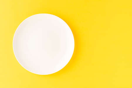 Overhead shot of blank white plate on yellow background. Flat lay