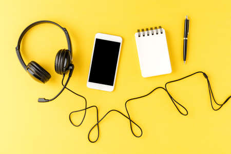 Helpdesk headset with phone, notebook and pen on yellow desktop. Call centerの写真素材