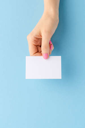 Female hand holding a mockup of a business card on blue background. Close upの写真素材