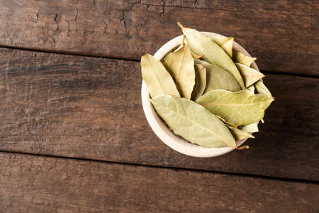 Dried bay leaves in bowl on wooden table. Close up. Top viewの写真素材