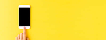 Woman's hand using smart phone with empty screen on yellow background. bannerの写真素材
