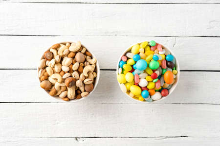 Diet decision concept. Mixed nuts and sweet in bowls on white wooden background. Top viewの写真素材
