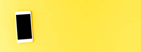 Smartphone with empty screen on yellow desktop. Banner. Top view