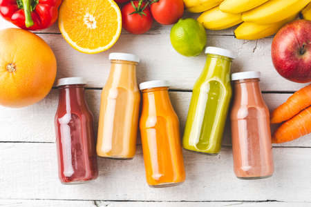 Multicolored juices in bottles on white wooden background with fruits and vegetables. Top viewの写真素材