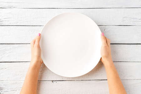 Overhead shot of female hands holding empty white plate over wooden background. Close upの写真素材