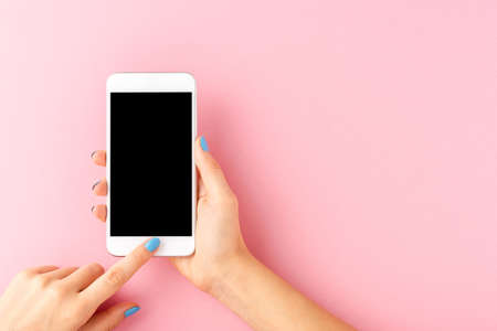 Woman's hand with blue nails holding mobile phone with empty screen on pink background. Top viewの写真素材