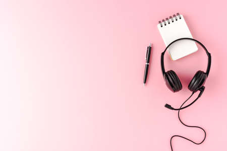 Help desk headset with notebook and pen on pink desktop with copyspace. Call center concept. Top viewの写真素材