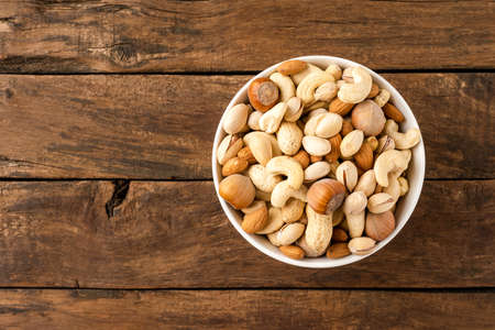 Nuts: almonds, pistachios, peanuts, hazelnuts and cashews in bowl on wooden background with copyspaceの写真素材