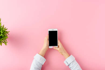 Young woman using mobile phone over pink table. Office desktop. Top viewの写真素材