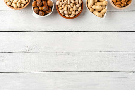 Overhead shot of different nuts in bowls on white wooden background with copyspace. Close up