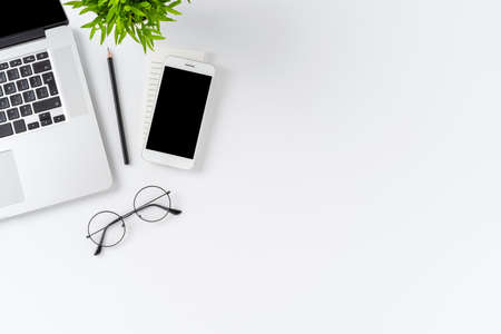 Office desktop with laptop, mobile phone and eyeglasses on white background with copyspace. Flat layの写真素材