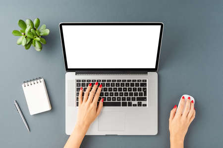 Female hands working on laptop with empty display. Office desktop with accessories. Top view