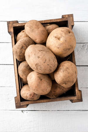 Overhead shot of uncooked potatoes in box on white wooden background. Top view. Close upの写真素材