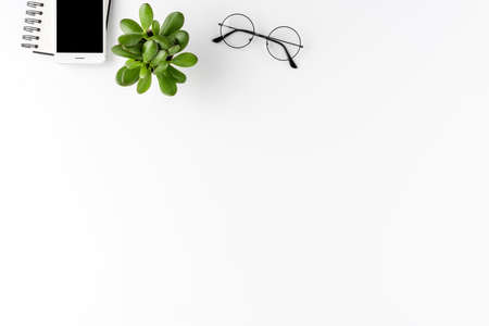 Elegant office desktop with mobile phone, notebook, eyeglasses and small plant. Business background...