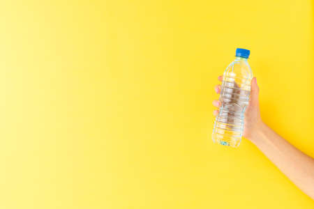 Woman's hand holding small plastic bottle of water on yellow background with copyspaceの写真素材