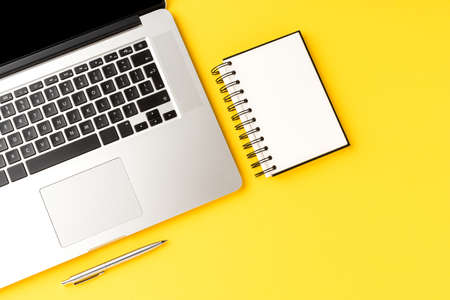 Office desktop with laptop, notebook and pen on yellow background with copyspace. Modern workplaceの写真素材