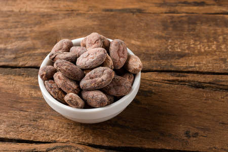 Cocoa beans in bowl on vintage wooden tableの写真素材