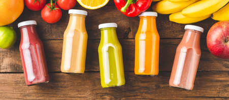 Multicolored juices in bottles on old wooden background with fruits and vegetables. Top view. Bannerの写真素材
