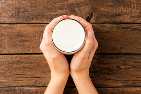 Overhead shot of woman's hands holding glass of milk on rustic wooden tableの写真素材