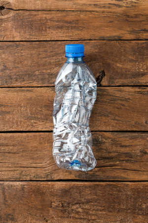 Used and crushed small bottle of water with cap on rustic wooden background. Plastic recycling. Top viewの写真素材
