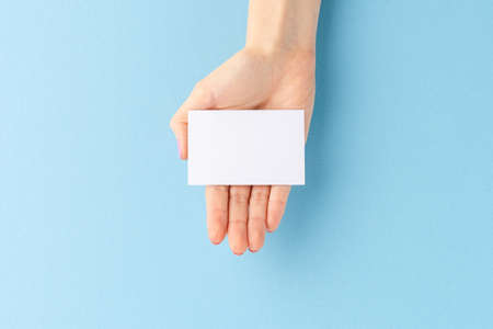 Woman's hand holding empty business card on blue background. Close upの写真素材