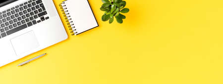 Office desktop with laptop, mobile phone, notebook and pen on yellow background with copyspace. Modern workplace. Bannerの写真素材