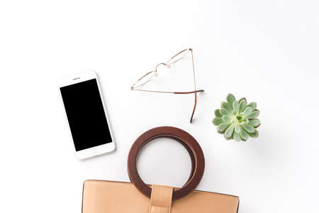 Concept of woman's purse, phone, eyeglasses and small flower isolated on white table. Fashion background. Top viewの写真素材