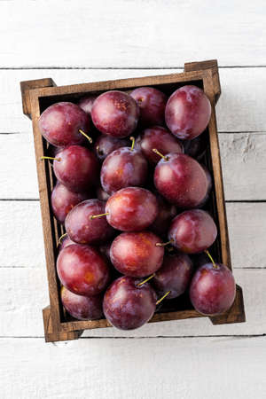 Overhead shot of plums in box on white wooden table. Close upの写真素材