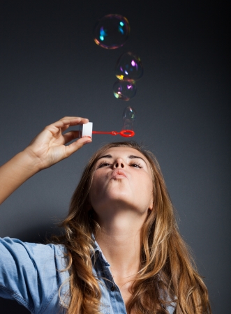 Beautiful young girl blowing soap bubbles on dark backgroundの写真素材