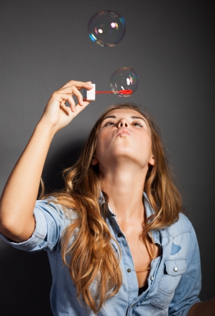 Beautiful young girl blowing soap bubbles on dark backgroundの写真素材