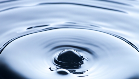 Water splash close up with ripples, clean blue background