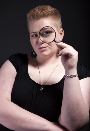 Chubby woman with short hair looking through a magnifying glass with eyeの写真素材
